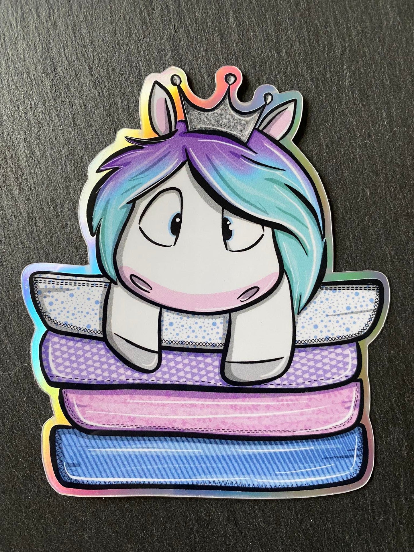 A holographic sticker featuring a colorful cartoon unicorn with a crown, horn, and eyes, on a background with geometric patterns.